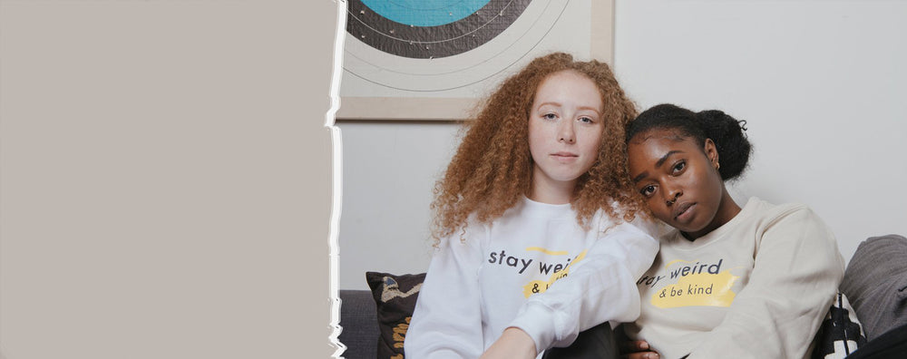 Two girls in Scoria sweatshirts that say Stay Weird and Be Kind